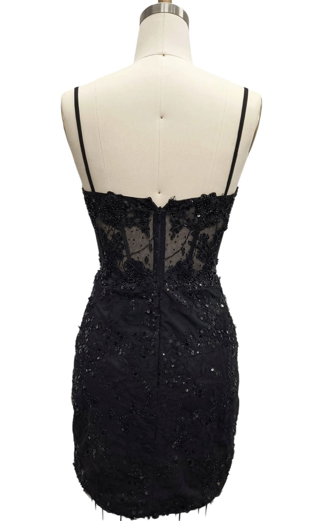 Back view of the Short Black Sequin Hoco Dress: 12660—this sleeveless mini dress features thin straps, a sheer lace upper panel, and sparkling sequin embellishments, shown on a dress form.